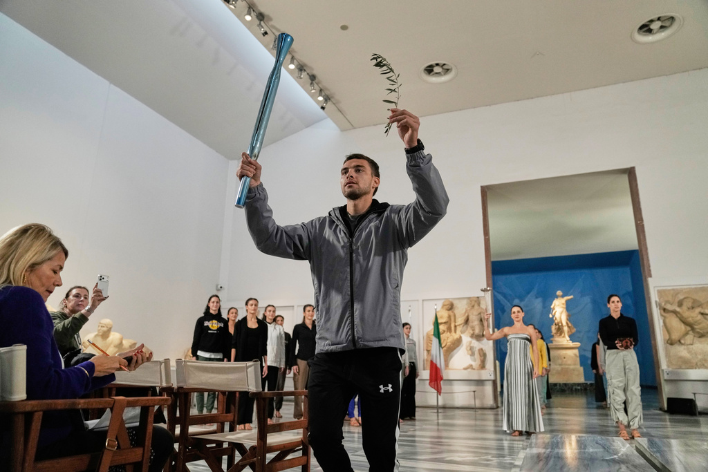 Greek rower and bronze medalist Petros Gaidatzís holds a torch and a olive branch during the final rehearsal ahead of the flame lighting for the Milan Cortina 2026 Winter Olympics, at the archaeological museum of Olympia, Greece, Tuesday, Nov. 25, 2025. (AP Photo/Thanassis Stavrakis)
