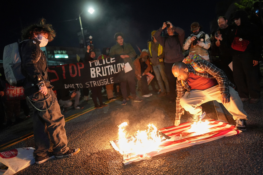 A protester burns an American flag in front of the Metropolitan Detention Center for the Federal Bureau of Prisons during a protest in Los Angeles, Thursday, Jan. 8, 2026, following the death of Renee Good, who was fatally shot by an ICE officer. (AP Photo/Jae C. Hong)