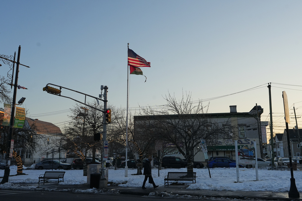 A man walks near flags of the United States and Palestine as the sun sets in "Palestine Way," a section of Main Street in Paterson, N.J. during Ramadan on Friday, Feb. 27, 2026. (AP Photo/Luis Andres Henao)