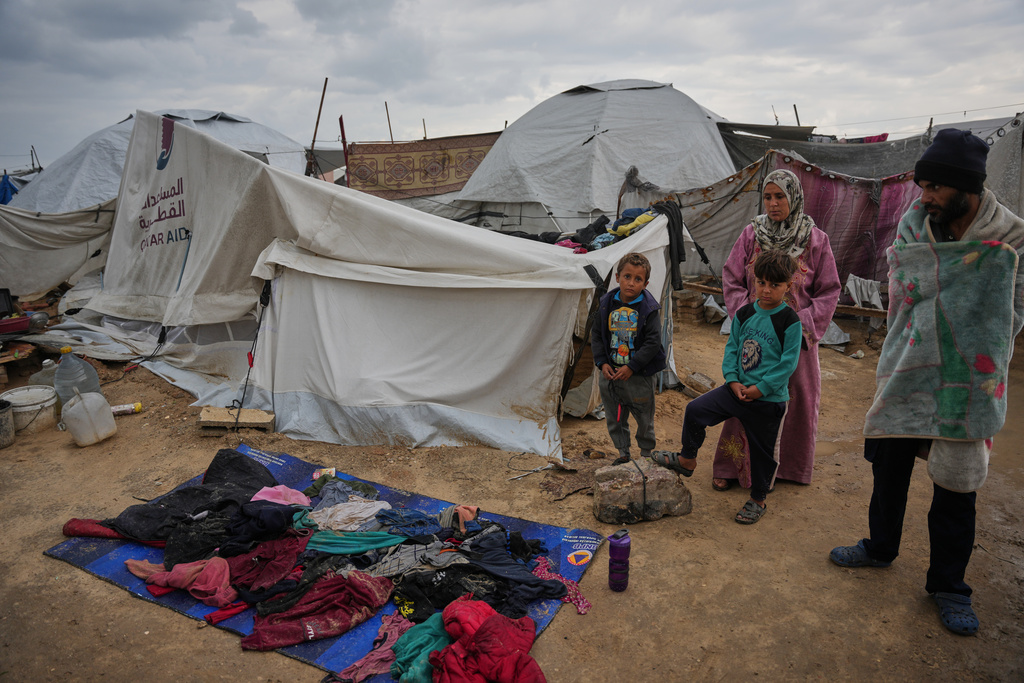 Raafat Alwan, 32, right, and his family stand outside their tent as their clothes lie over a tarp to dry in a makeshift camp for displaced Palestinians set up on the beach during a cold morning in Gaza City, Tuesday, Dec. 16, 2025. (AP Photo/Abdel Kareem Hana)