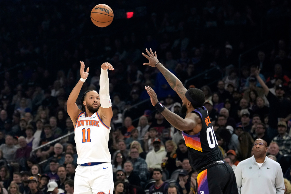 New York Knicks guard Jalen Brunson (11) shoots a 3-pointer over Phoenix Suns forward Royce O'Neale during the first half of an NBA basketball game, Friday, Jan. 9, 2026, in Phoenix. (AP Photo/Ross D. Franklin)