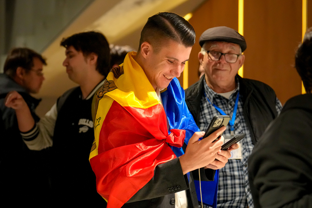 A supporter of the pro-EU Party of Action and Solidarity (PAS) draped in the Moldovan flag smiles as he checks partial results on a phone after the polls closed for the parliamentary election, in Chisinau, Moldova, Sunday, Sept. 28, 2025. (AP Photo/Vadim Ghirda)