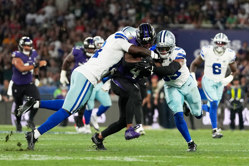 Baltimore Ravens wide receiver Zay Flowers (4) is tackled by Dallas Cowboys safety Markquese Bell (14) and linebacker Dee Winters (53) during the first half of an NFL football game in Rio de Janeiro, Sunday, Sept. 27, 2026. (AP Photo/Andre Penner)