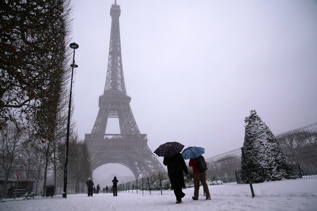 People walk near the Eiffel Tower during a snowfall Wednesday, Jan. 7, 2026 in Paris. (AP Photo/Christophe Ena)
