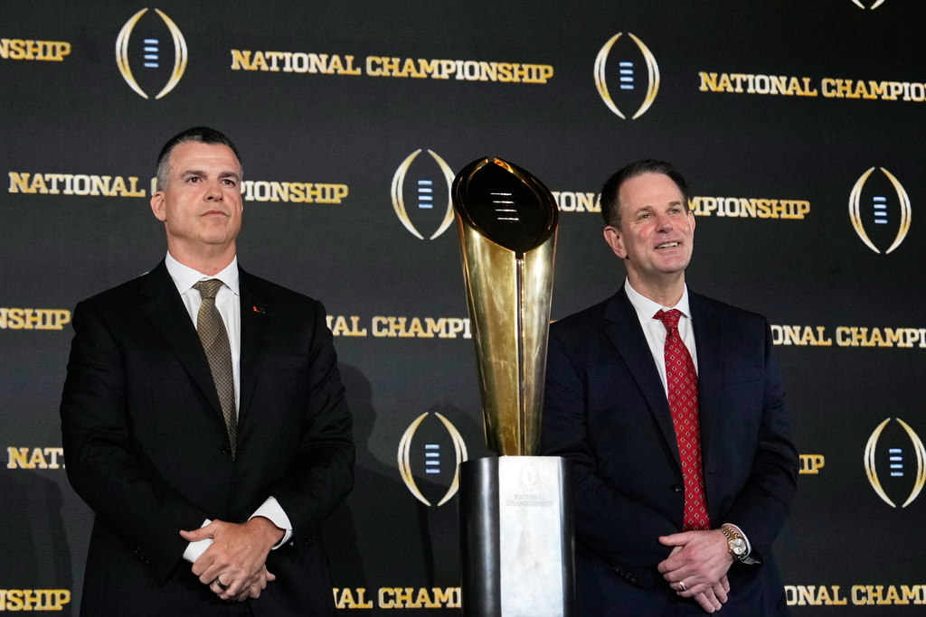 Miami head coach Mario Cristobal and Indiana head coach Curt Cignetti pose with the trophy after a news conference ahead of the College Football Playoff national championship game between Miami and Indiana, Sunday, Jan. 18, 2026, in Miami. The game will be played on Monday. (AP Photo/Chris Carlson)