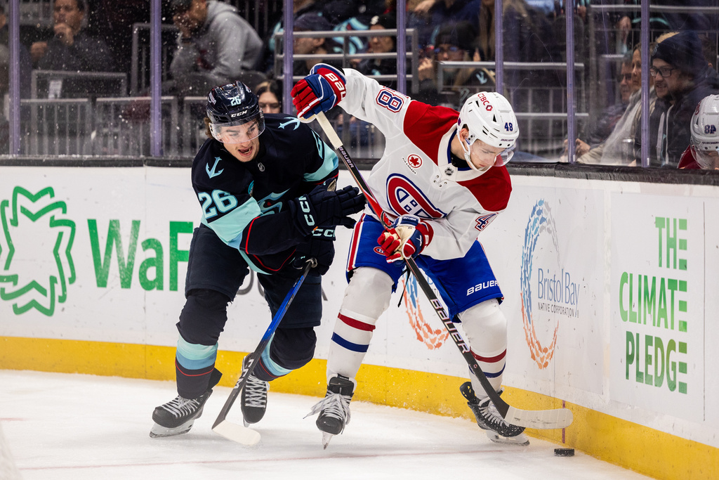 Seattle Kraken center Ryan Winterton, left, and Montreal Canadiens defenseman Lane Hutson, right, fight for the puck during the second period of an NHL hockey game Tuesday, Oct. 28, 2025, in Seattle. (AP Photo/Maddy Grassy)