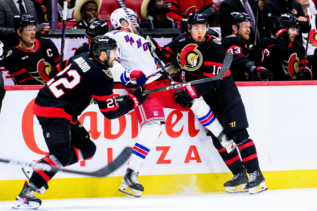 Ottawa Senators' Jordan Spence (10) holds New York Rangers' Alexis Lafreniere, center, against the boards during second-period NHL hockey game action in Ottawa, Ontario, Thursday, Dec. 4, 2025. (Spencer Colby/The Canadian Press via AP)