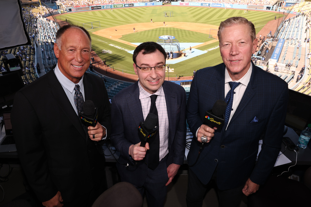 This photo provided by NBC Sports shows NBC “Sunday Night Baseball” play-by-play announcer Jason Benetti, center, standing with former Arizona Diamondbacks player Luis Gonzalez, left, and former Los Angeles Dodgers pitcher Orel Hershiser, right, before a baseball game on March 26, 2026, in Los Angeles. (Jesse Grant/NBC Sports via AP)