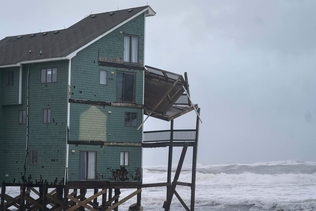 A balcony hangs off a home at risk of collapse in the midst of a storm, Sunday, Oct. 12, 2025, in Buxton, N.C. (AP Photo/Allison Joyce)