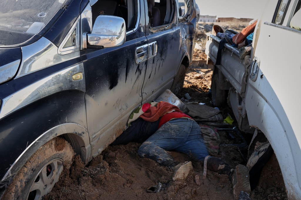 The body of a civilian lies in between two trucks along a road between government-controlled Raqqa and SDF-controlled Hassakeh in northeastern Syria, Tuesday, Jan. 20, 2026. (AP Photo/Omar Albam)