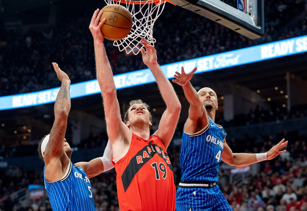 Toronto Raptors centre Jakob Poeltl (19) drives to the hoop past Orlando Magic guard Jalen Suggs (4) and forward Paolo Banchero (5) during first half NBA action in Toronto on Sunday, March 29, 2026. (Frank Gunn/The Canadian Press via AP)