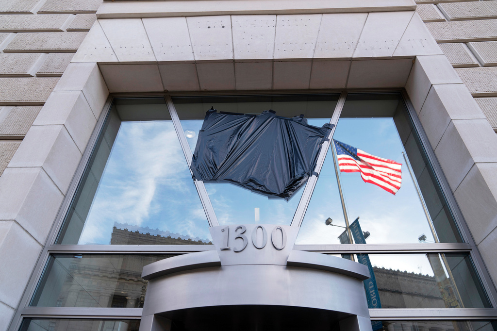 FILE - The American flag flying alone beside an empty flagpole that previously had the flag of the U.S. Agency for International Development, or USAID, are pictured in the reflection of a window that previously had the sign and the seal of USAID, outside the agency's headquarters in Washington, Feb. 7, 2025. (AP Photo/Jose Luis Magana, File)