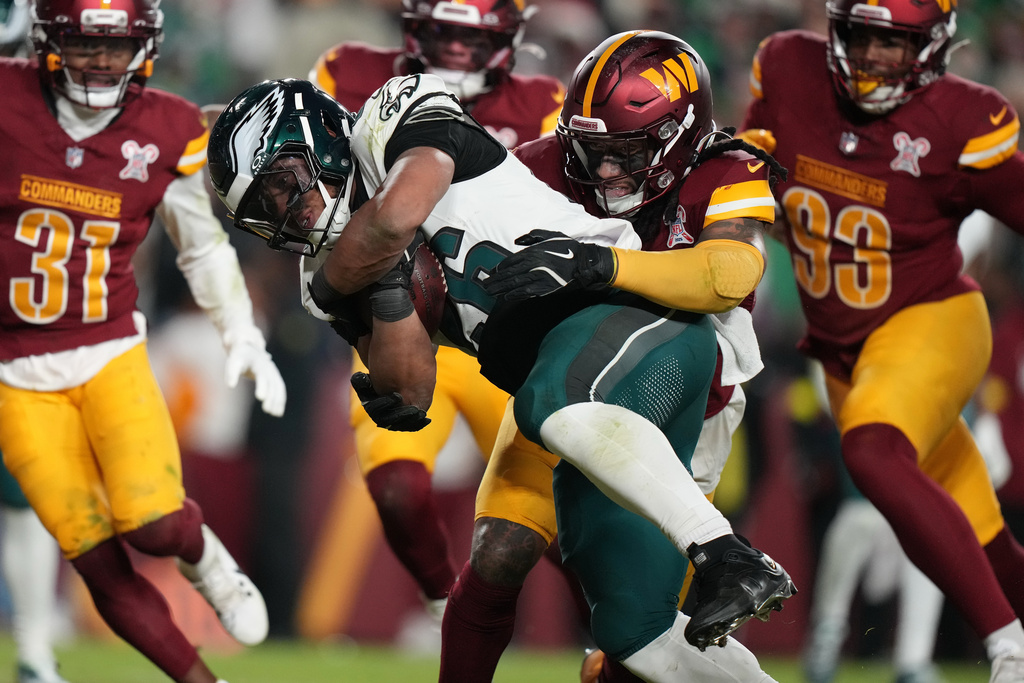Philadelphia Eagles running back Saquon Barkley, center left, runs for a touchdown against Washington Commanders cornerback Noah Igbinoghene, center right, during the second half of an NFL football game, Saturday, Dec. 20, 2025, in Landover, Md. (AP Photo/Stephanie Scarbrough)