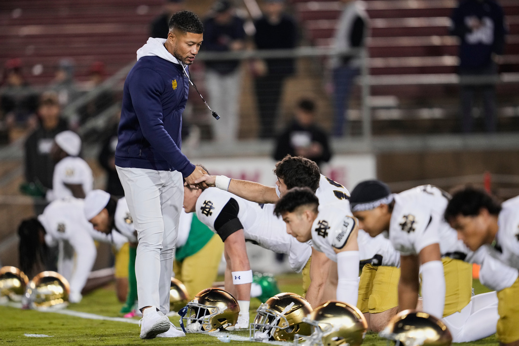 Notre Dame head coach Marcus Freeman, left, shakes hands with players as they warm up before an NCAA college football game against Stanford, Saturday, Nov. 29, 2025, in Stanford, Calif. (AP Photo/Godofredo A. Vásquez)