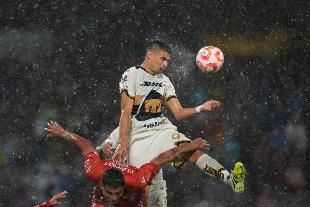 Rain pours down as Pumas' Guillermo Martínez heads the ball over Necaxa's Tomas Badaloni during a Mexican soccer league match in Mexico City, Aug. 10, 2025. (AP Photo/Fernando Llano)