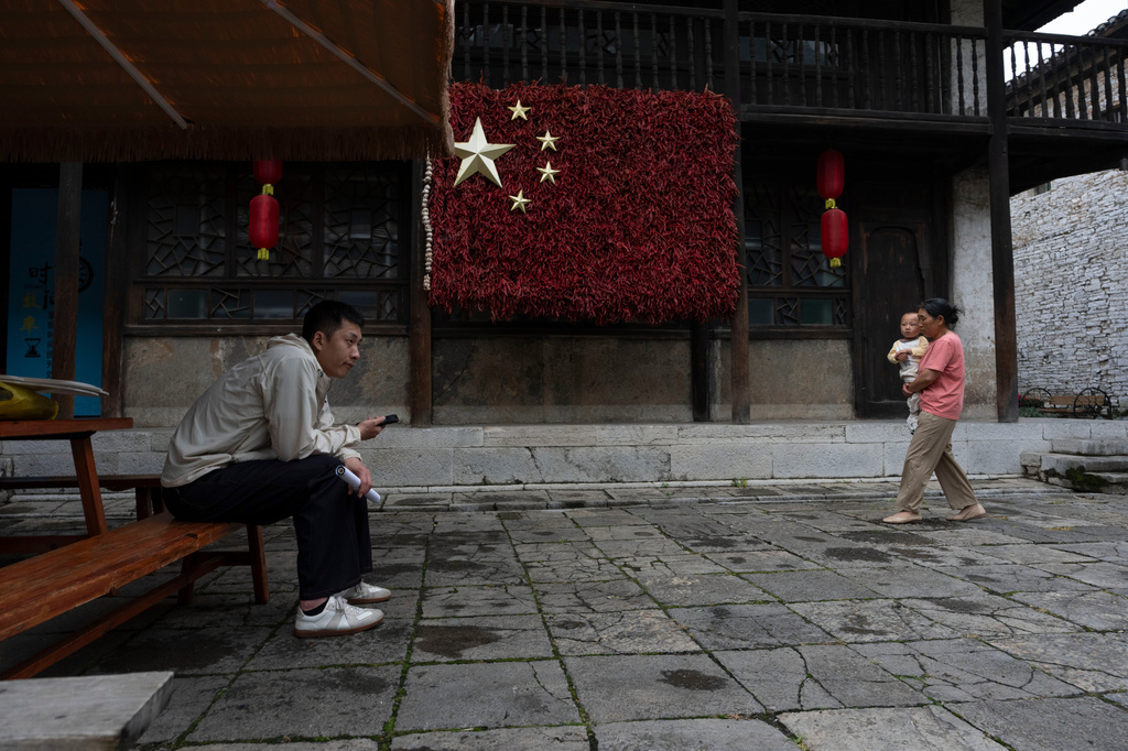 A woman walks with a child past a Chinese national flag made from dried chili at Tianlong Tunpu, an ancient town in southwestern China's Guizhou province on Thursday, May 28, 2026. (AP Photo/Ng Han Guan)
