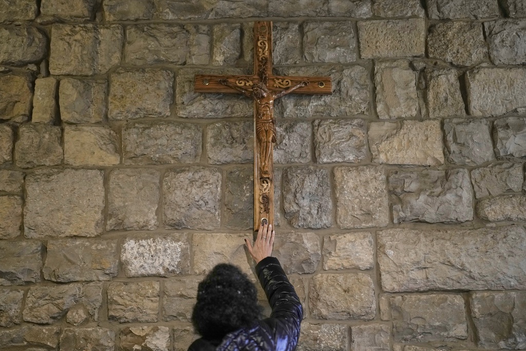 A worshipper touches a wooden crucifix inside the shrine of St. Charbel in the northern village of Annaya, Lebanon, Saturday, Nov. 15, 2025. (AP Photo/Hassan Ammar)