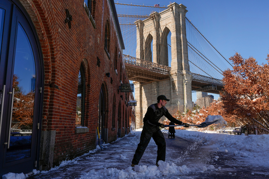 A worker clears snow outside the Empire Stores building in Brooklyn Bridge Park, Tuesday, Feb. 24, 2026, in the Brooklyn borough of New York. (AP Photo/Yuki Iwamura)