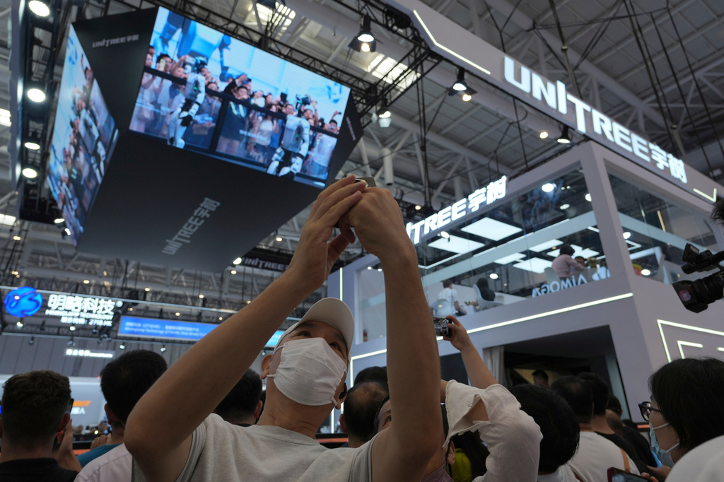Visitors to the World Robot Conference take selfies near the Unitree booth in Beijing, on Aug. 20, 2026. (AP Photo/Ng Han Guan)