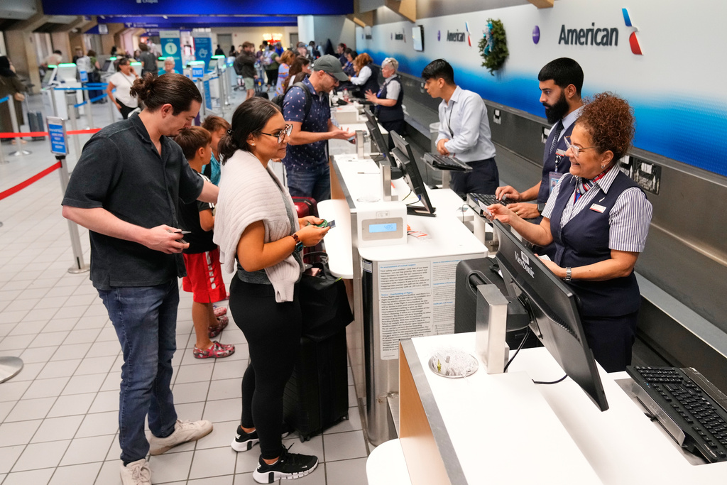 Myrna Santiago, right, a customer service agent with American Airlines, assists travelers at a ticketing gate at the Dallas Fort Worth International Airport, at DFW Airport, Texas, Friday, Nov. 21, 2025. (AP Photo/Tony Gutierrez)