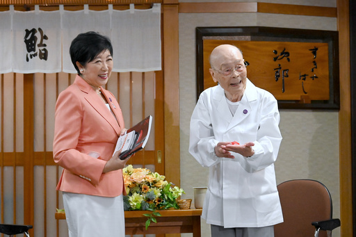 In this photo released by Bureau of Social Welfare, Tokyo Metropolitan Government, sushi legend Jiro Ono, right, shows a gift from Tokyo Gov. Yuriko Koike to celebrate his 100th birthday in front of his restaurant, Sukiyabashi Jiro in Tokyo on Sept. 18, 2025. (Bureau of Social Welfare, Tokyo Metropolitan Government via AP) In this photo released by Bureau of Social Welfare, Tokyo Metropolitan Government, sushi legend Jiro Ono, right, shows a gift from Tokyo Gov. Yuriko Koike to celebrate his 100th birthday in front of his restaurant, Sukiyabashi Jiro in Tokyo on Sept. 18, 2025. (Bureau of Social Welfare, Tokyo Metropolitan Government via AP)