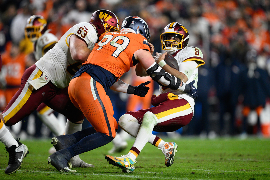 Washington Commanders quarterback Marcus Mariota (8) is hit by Denver Broncos defensive lineman Zach Allen (99) during the first half of an NFL football game Sunday, Nov. 30, 2025, in Landover, Md. (AP Photo/Nick Wass)