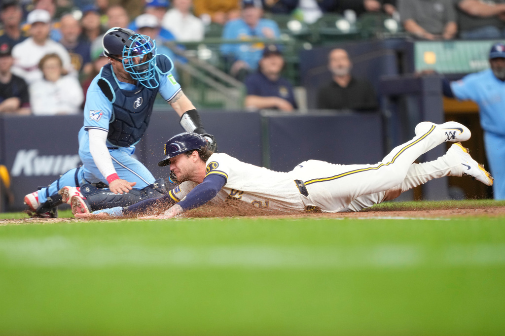 Milwaukee Brewers' Brice Turang, right, scores ahead of the tag by Toronto Blue Jays catcher Tyler Heineman, left, on a sacrifice fly hit by Luis Rengifo during the fourth inning of a baseball game, Thursday, April 16, 2026, in Milwaukee. (AP Photo/Kayla Wolf)