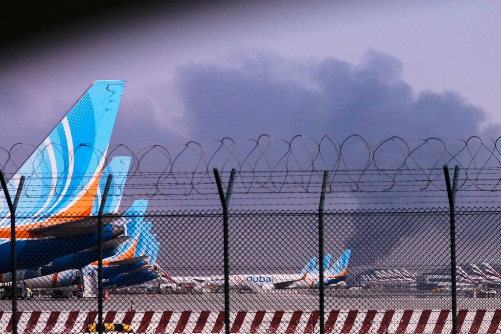 FlyDubai planeS is parked at Dubai International Airport as smoke rises in the background after a drone struck a fuel tank early morning, forcing the temporary suspension of flights, in Dubai, United Arab Emirates, Monday, March 16, 2026. (AP Photo)