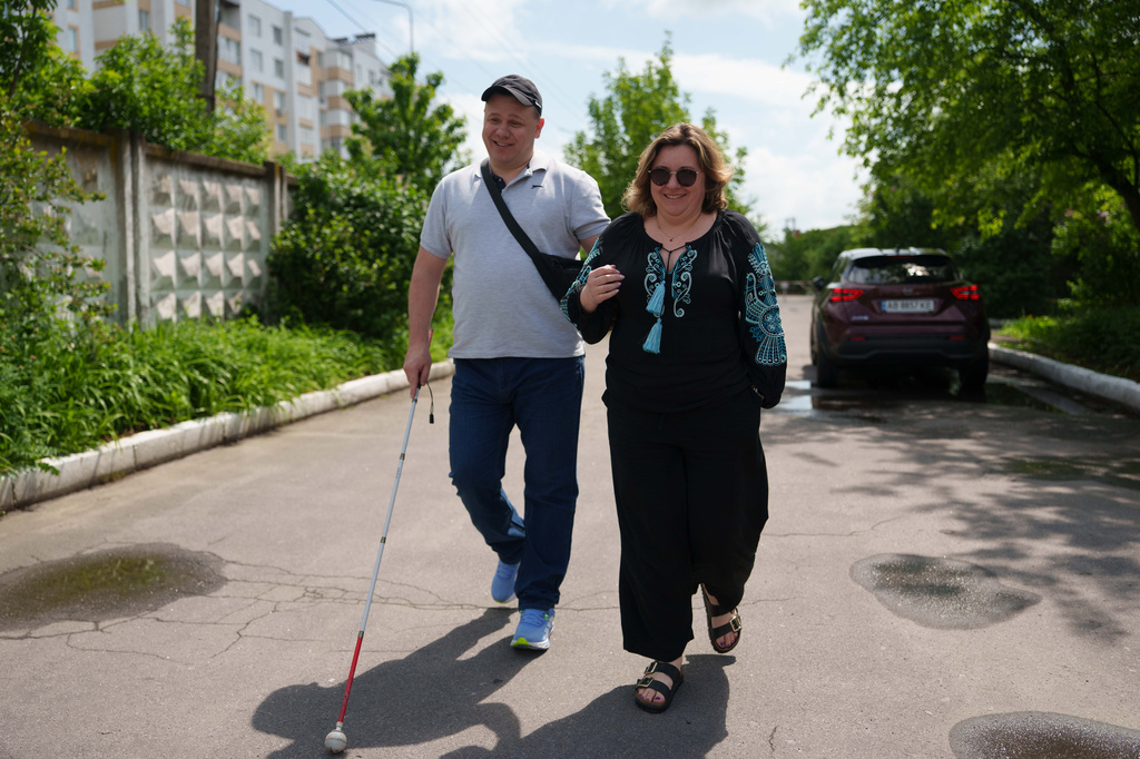 Ivan Shostak, left, a blind Ukrainian war veteran and Anastasia Lanina, community development officer of UNDP walk on a street in Vinnytsia, Ukraine, on May 21, 2026. (AP Photo/Evgeniy Maloletka)