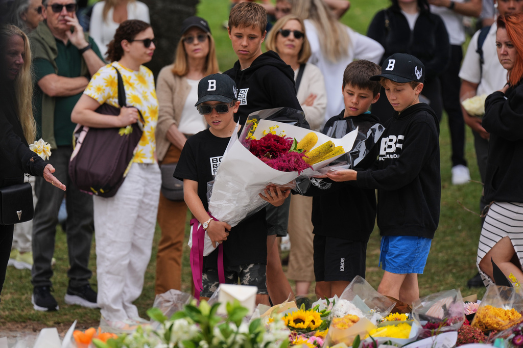 Boys lay flowers at a flower memorial for victims of Sunday's shooting at the Bondi Pavilion at Bondi Beach on Tuesday, Dec. 16, 2025, in Sydney, Australia. (AP Photo/Mark Baker)