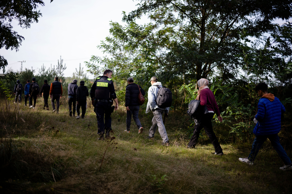 FILE - A Federal Police officer escorts a group of migrants who illegally crossed the border from Poland into Germany during a patrol in a forest near Forst, southeast of Berlin, Germany, on Oct. 11, 2023. (AP Photo/Markus Schreiber, File)