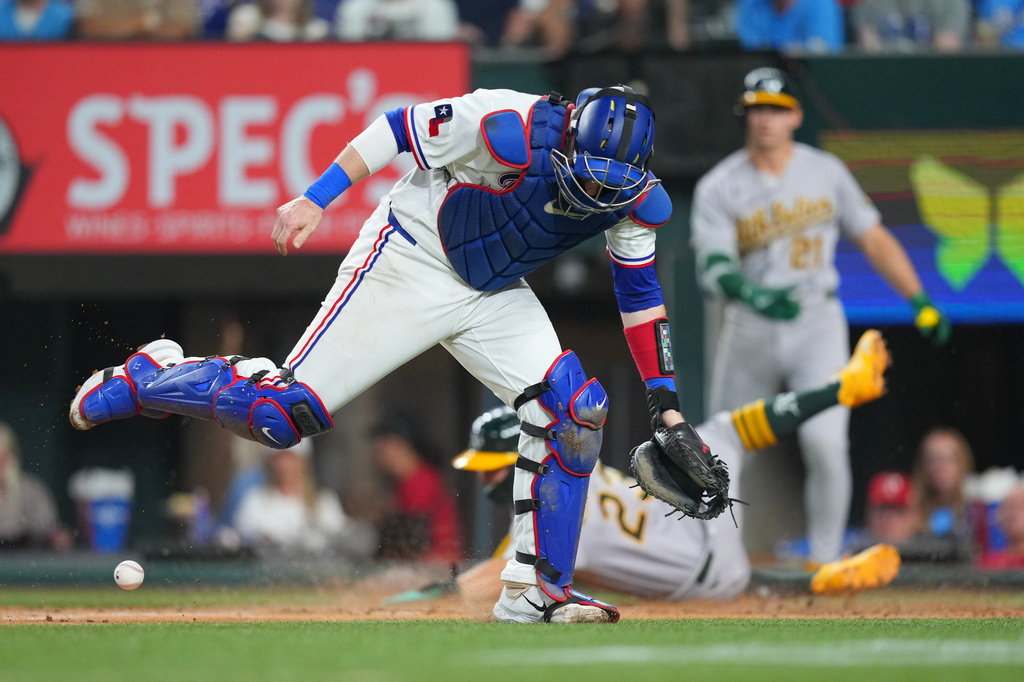 Texas Rangers catcher Danny Jansen, front, tries to get the ball as Athletics' Shea Langeliers, middle, slides onto home to score on a hit by Athletics's Colby Thomas during the third inning of a baseball game Saturday, April 25, 2026, in Arlington, Texas. (AP Photo/Julio Cortez)