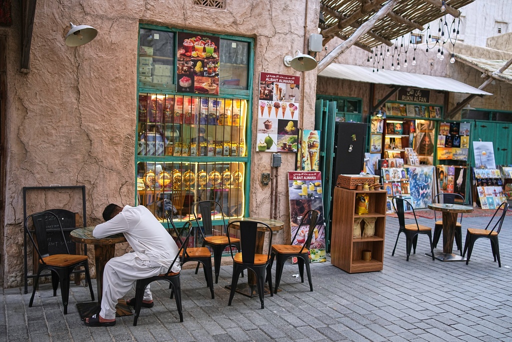 A man naps on a cafe table at the empty Al Seef market, next to the historic Al Fahidi neighborhood along Dubai Creek, one of the main tourist areas of Dubai, United Arab Emirates, Friday, March 13, 2026, as tourism slows amid regional tensions linked to the Iran war. (AP Photo/Fatima Shbair)