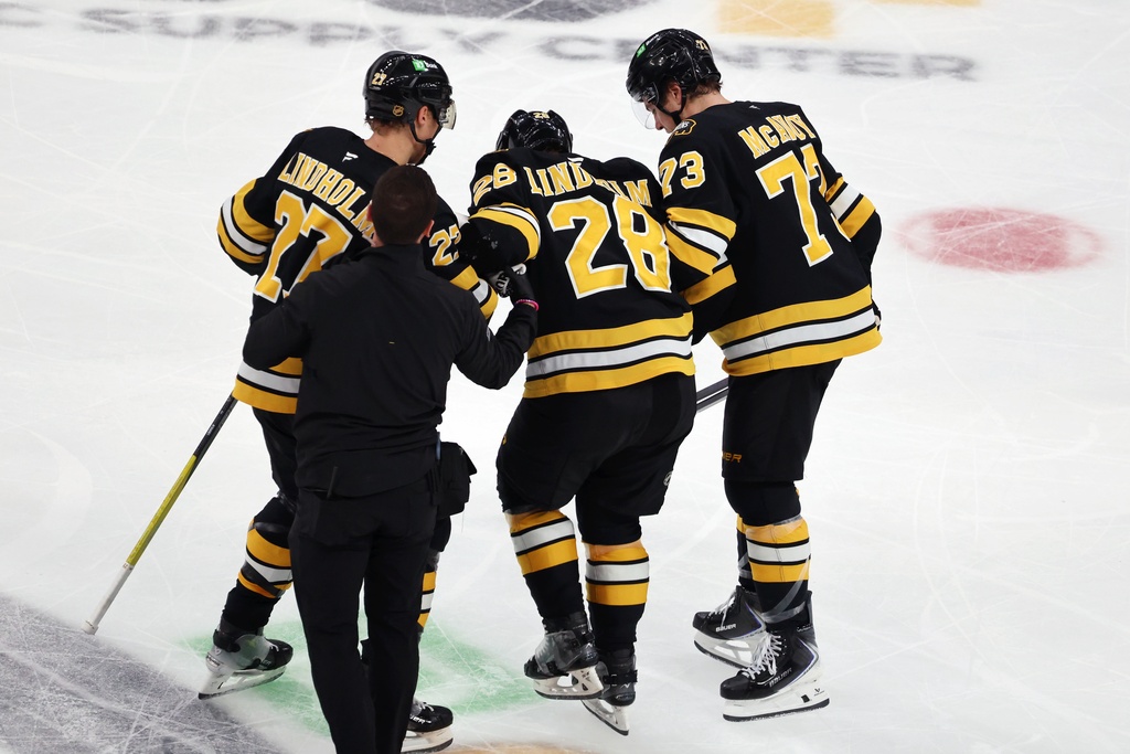 Boston Bruins' Hampus Lindholm (27) and Charlie McAvoy (73) help Elias Lindholm (28) off the ice during the second period of an NHL hockey game against the Buffalo Sabres, Thursday, Oct. 30, 2025, in Boston. (AP Photo/Michael Dwyer)