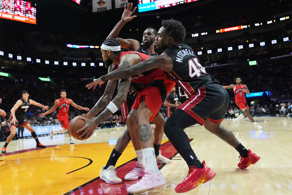 Miami Heat forward Andrew Wiggins, left, and guard Davion Mitchell (45) defend Toronto Raptors forward Brandon Ingram, center, during the second half of an NBA basketball game, Monday, Dec. 15, 2025, in Miami. (AP Photo/Lynne Sladky)
