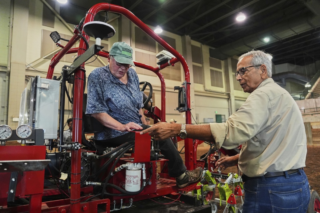 Farmer Vicki Morrane, left, listens as Ajit Srivastava, right, explains the mechanics of an electric tractor before she test drives Tuesday, Aug. 19, 2025, in East Lansing, Mich. (AP Photo/Joshua A. Bickel)