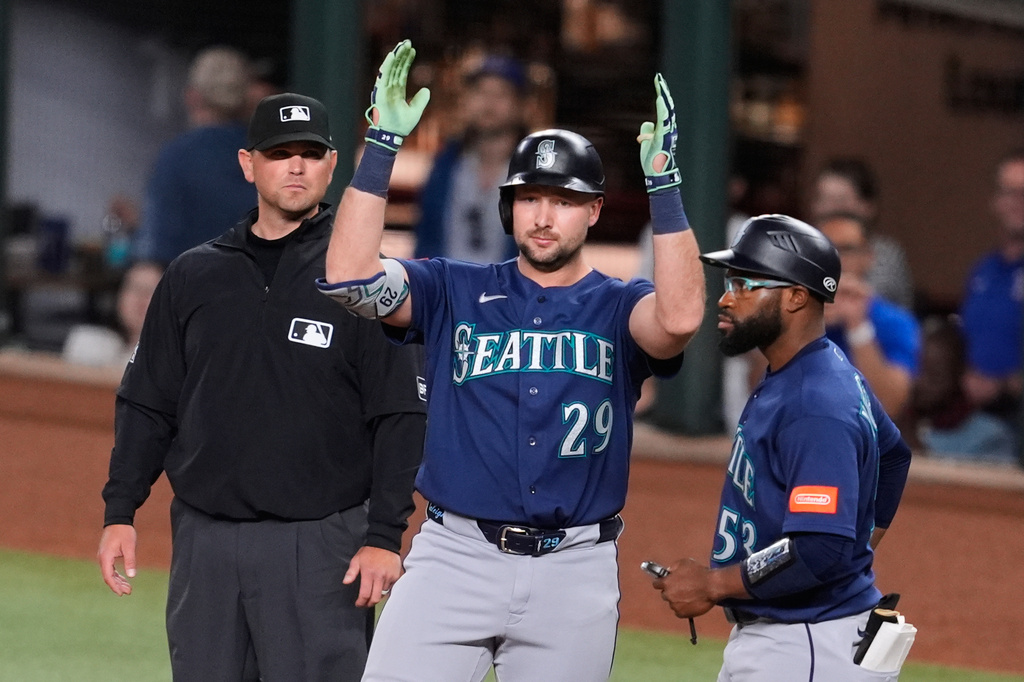 Seattle Mariners' Cal Raleigh (29) celebrates hitting a run-scoring single as first base coach Eric Young Jr., right, and umpire Brock Ballou, left, look on in the fifth inning of a baseball game against the Texas Rangers Tuesday, April 7, 2026, in Arlington, Texas. (AP Photo/Tony Gutierrez)