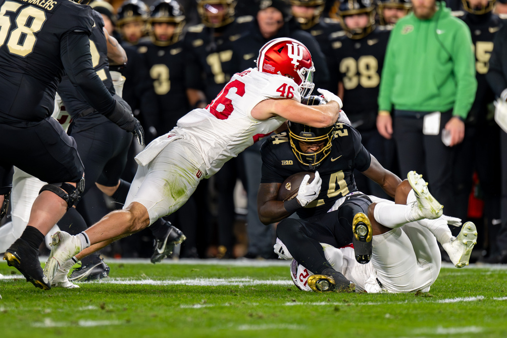 Purdue running back Malachi Thomas (24) is hit by Indiana linebacker Isaiah Jones (46) and defensive back Devan Boykin, bottom right, during the first half of an NCAA college football game, Friday, Nov. 28, 2025, in West Lafayette, Ind. (AP Photo/Doug McSchooler)