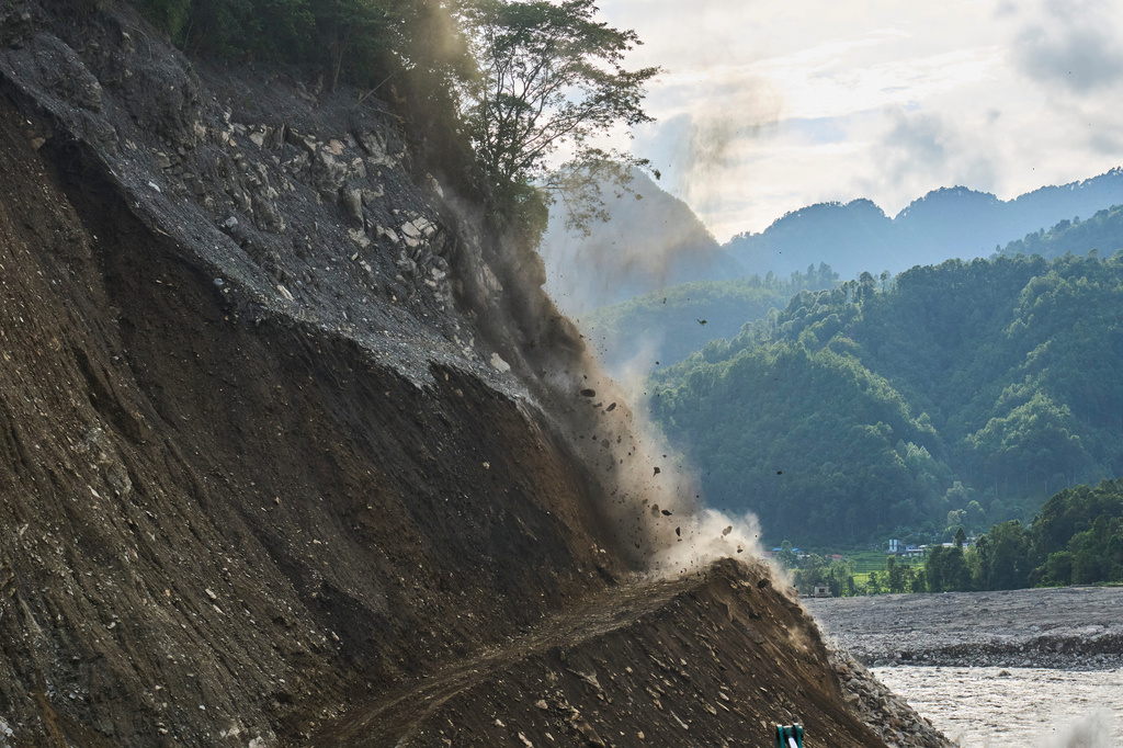 Rocks tumble from a hillside after controlled explosives are used to clear a route for a temporary road reconnecting towns and villages after flash floods damaged the existing road in Nepal's Nuwakot district, Wednesday, Sept. 23, 2026. (AP Photo/Niranjan Shrestha)