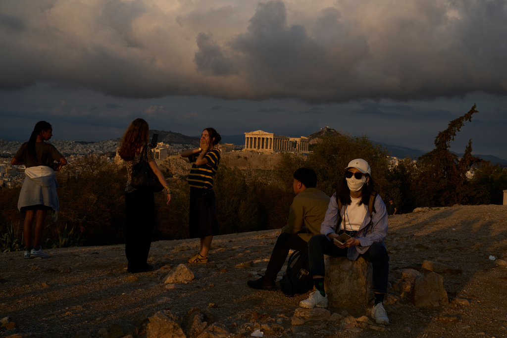 Tourists stand on Filopappos Hill with the ancient Parthenon temple atop the Acropolis hill in the background, in Athens, Tuesday, Oct. 21, 2025. (AP Photo/Petros Giannakouris)
