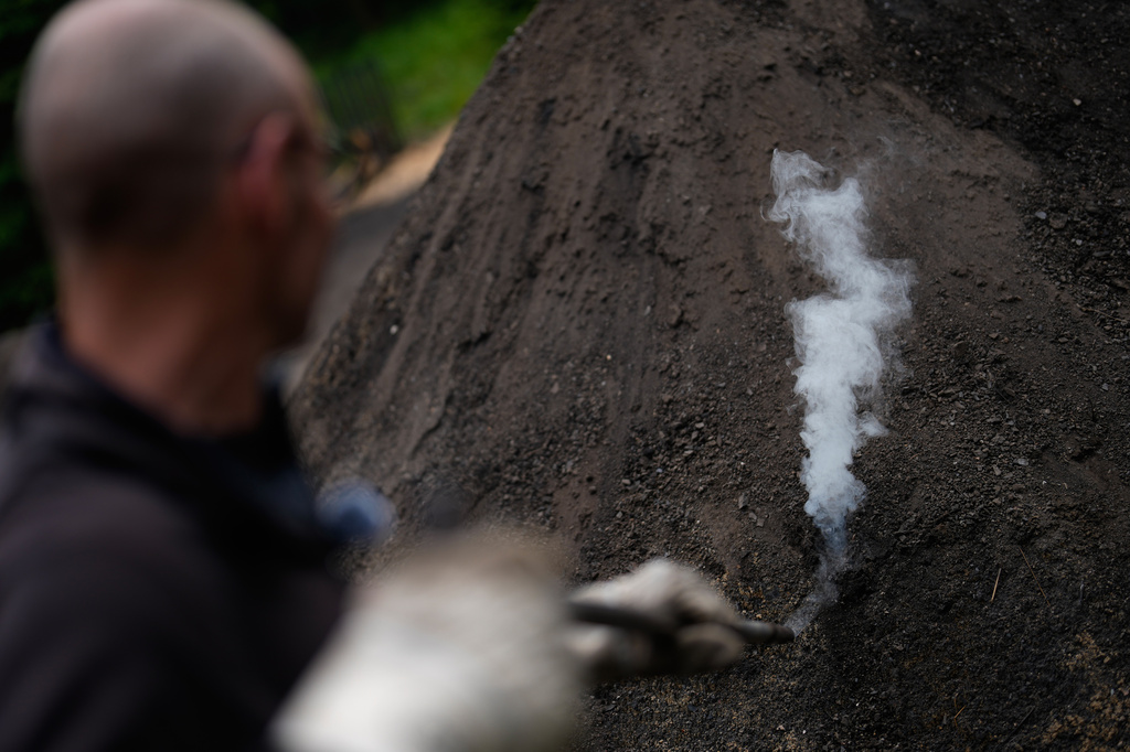 Immo Feldmer uses a pole to ventilate a mound of earth at his family-run, traditional charcoal production site near Hasselfelde in Germany's Harz forest, Wednesday, June 10, 2026. (AP Photo/Matthias Schrader)