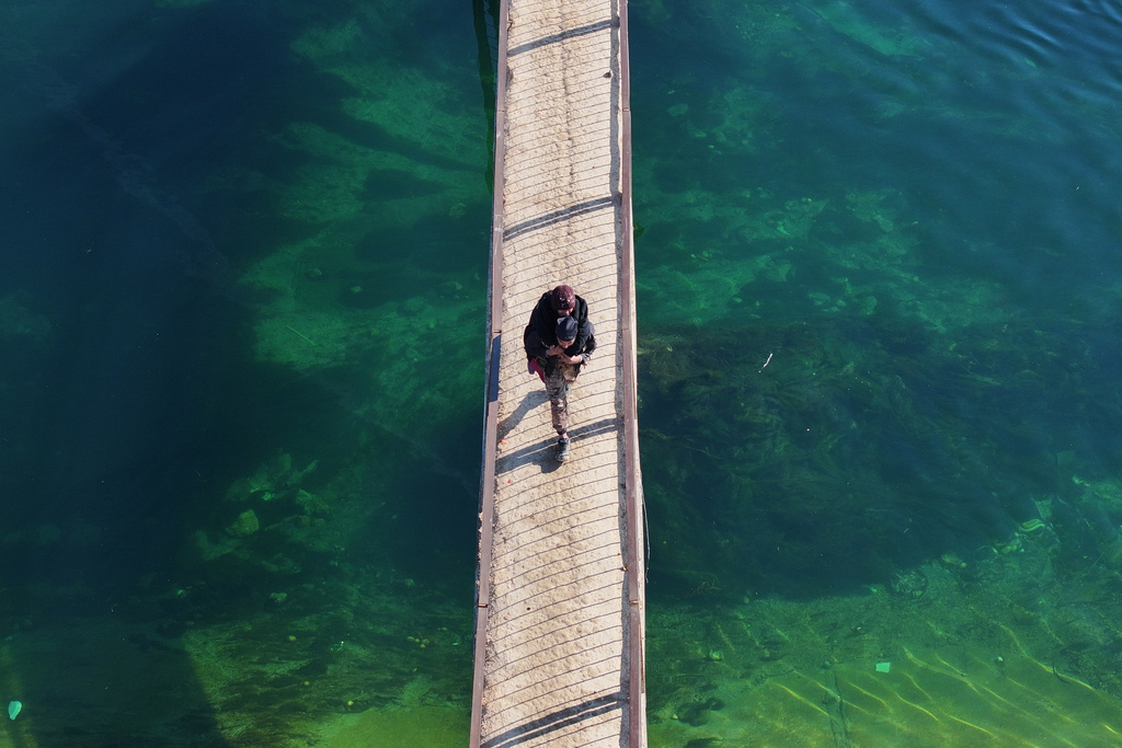 FILE - A man carries a woman as he walks on a bridge over a river near the village of Rasm al-Harmil al-Imam in the eastern Aleppo countryside, near the front line with the Kurdish-led Syrian Democratic Forces, in Deir Hafer, Syria, Friday, Jan. 16, 2026. (AP Photo/Ghaith Alsayed)