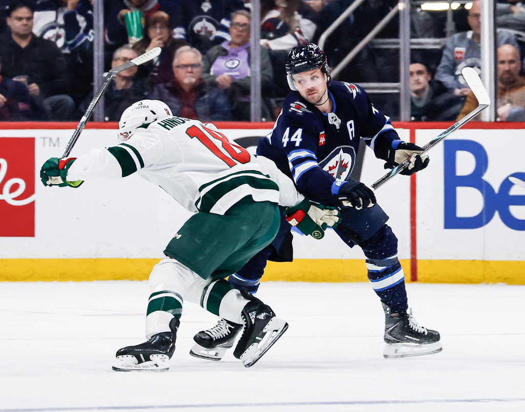 Winnipeg Jets' Josh Morrissey (44) defends against Minnesota Wild's Vincent Hinostroza (18) during second-period NHL hockey game action in Winnipeg, Manitoba, Saturday, Dec. 27, 2025. (John Woods/The Canadian Press via AP)