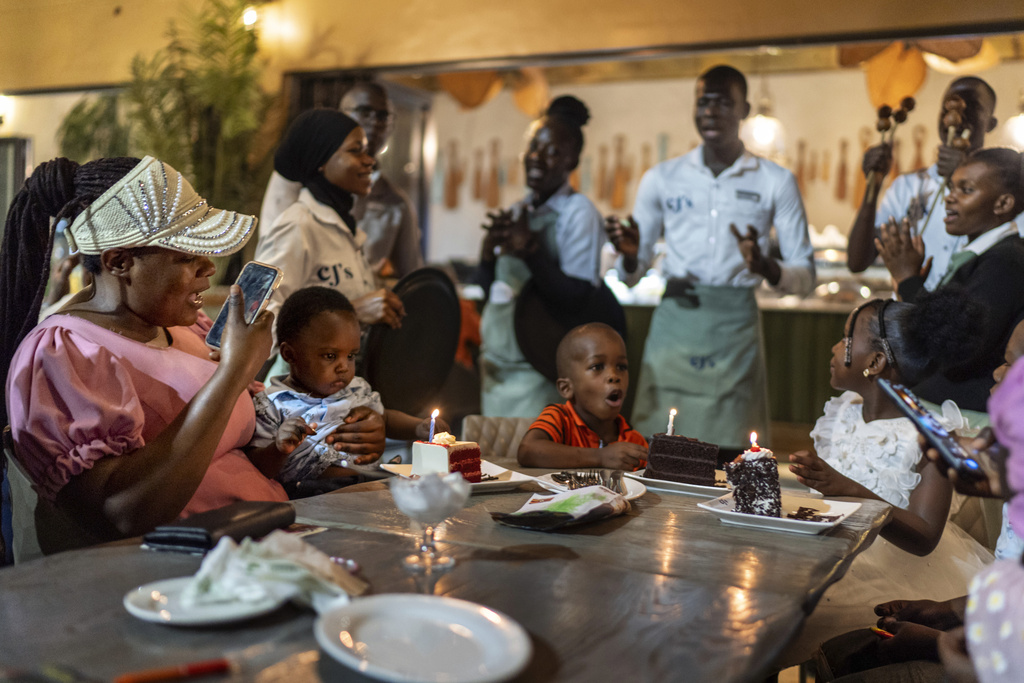Rose Nakirigya, left, holds her son, Axell, as he celebrates his 1st birthday with siblings, Abia, 4, and Ariel, 5, right, at a restaurant, Saturday, Nov. 23, 2024, in Kampala, Uganda. (AP Photo/David Goldman)