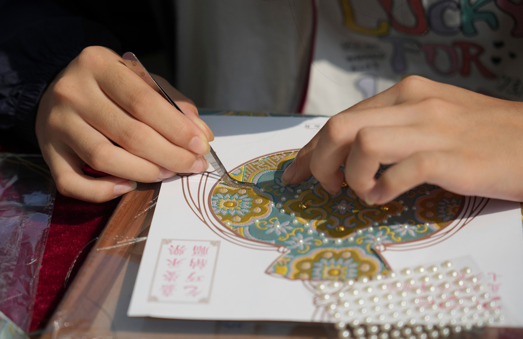 A child makes a sachet-shaped Song brocade pearl painting during a festival to celebrate Qixi at the Beijing Folk Custom Museum in Beijing, Wednesday, Aug. 19, 2026. (AP Photo/Achmad Ibrahim)