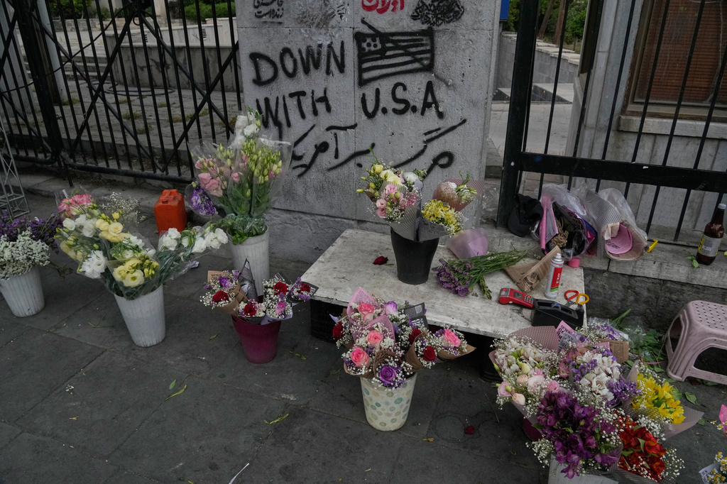 An anti-U.S. graffiti is painted on a wall as flowers are displayed by a street vendor in downtown Tehran, Iran, Sunday, May 24, 2026. (AP Photo/Vahid Salemi)