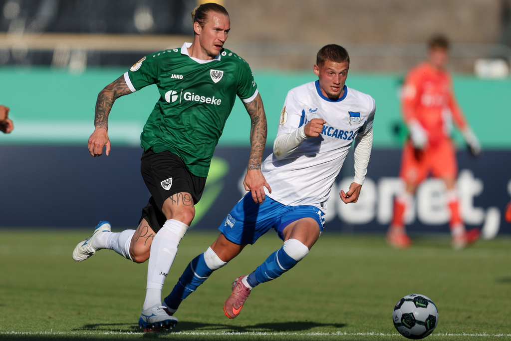 Hertha's Mickael Cuisance, right, and Muenster's Marvin Schulz, left, challenge for the ball during the German soccer cup first round match between Preussen Muenster and Hertha BSC in Muenster, Germany, Monday, Aug. 18, 2025. (Friso Gentsch/dpa via AP)