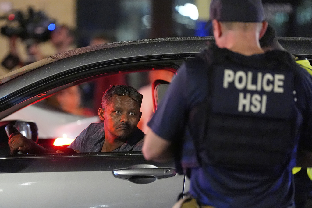 A driver peers from his window while a Department of Homeland Security agent and a city police officer conduct a traffic checkpoint along 14th Street in Washington, Aug. 13, 2025. (AP Photo/Alex Brandon)