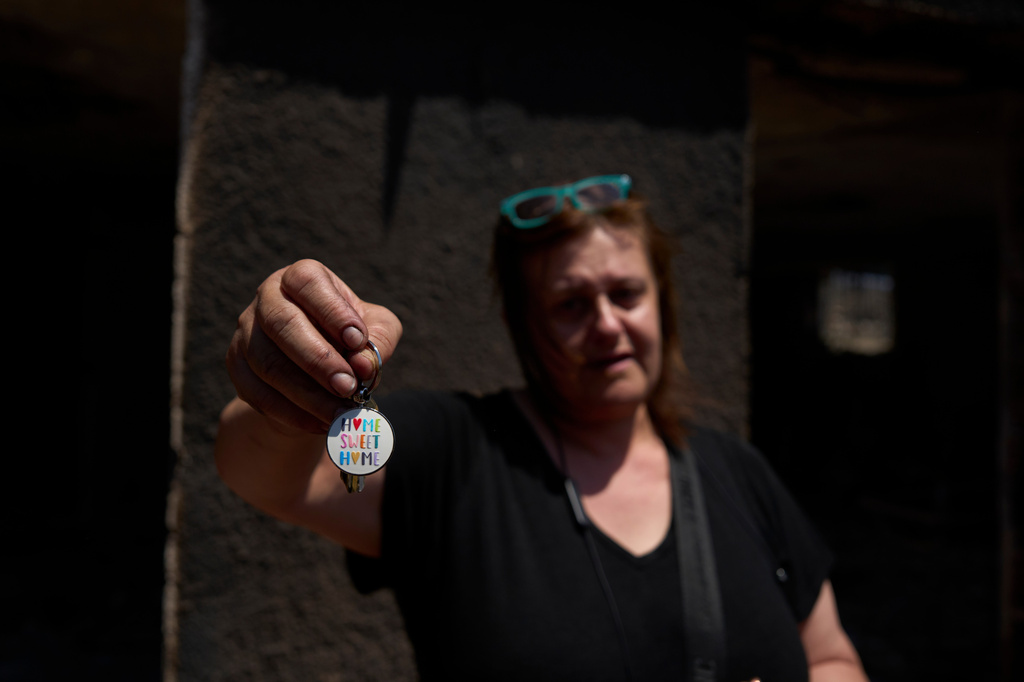 Evgenia Spanou holds the keys to her holiday home, attached to a "Home Sweet Home" keychain, outside the same house destroyed by a wildfire in Porto Germeno, northwest of Athens, Greece, Tuesday, Aug. 4, 2026. (AP Photo/Petros Giannakouris)