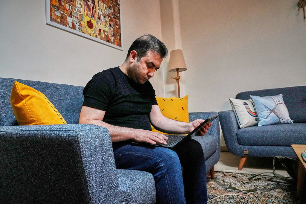 Mehdi Alishir looks at his laptop in his living room in Tehran, Iran, Sunday, April 5, 2026. (AP Photo/Vahid Salemi)